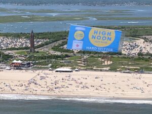 Aerial billboard featuring the alcoholic beverage brand High Noon flying over a New York beach in Long Island.