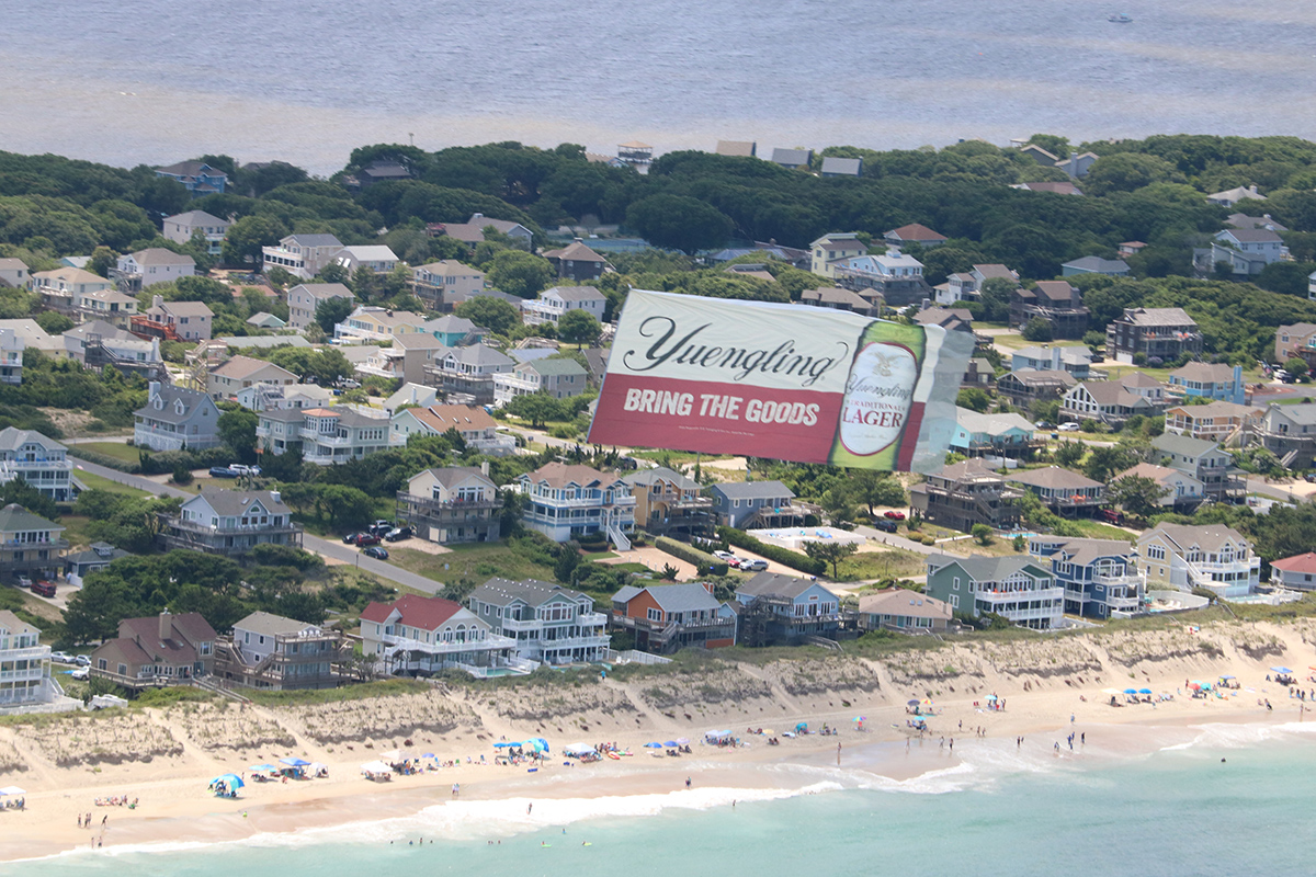 Beer ad over coastal homes, Beachfront brewery banner flyby
